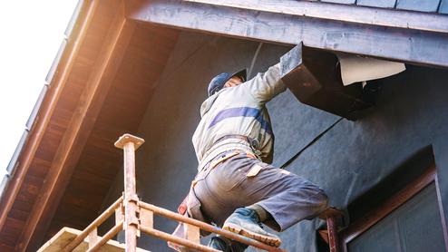 Arbeiter steht auf einem Gerüst und befestigt ein Element unter dem Dach eines Hauses.
